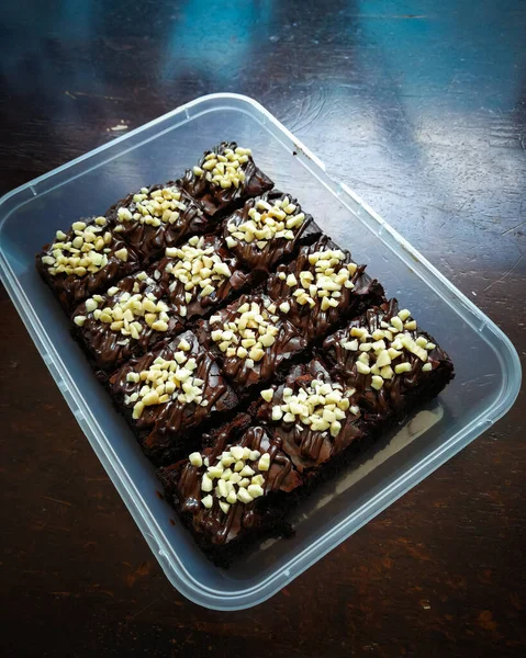 Tahta arka planda, üzerinde badem uçları, ev yapımı fırın ve tatlı olan plastik bir kapta çikolatalı brownie.