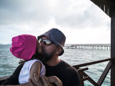 Lüks tatil köyü, mutlu aile rahatlaması. Babam ve yeni yürümeye başlayan çocuk su dağ evi tatil köyünün güvertesinde oturuyor. Yaz tatili fikri.