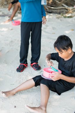 Çocuk sahilde piknik yaparken beslenme çantasından yemek yiyor..