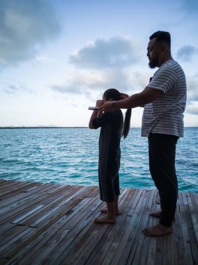 Sevgi dolu bir aile. Baba, kızının saçını tarıyor. Denize karşı duran bir güvertede..