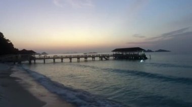 Arka planda iskeleyle birlikte ada sahiline su sıçrayan deniz dalgaları. Güzel gündoğumunda kumsalda su sıçratmak.