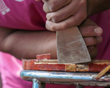 Eski masa temizleme sözcüsünün elinde skapele, egzotik ahşap talaş tahtası talaşı var.