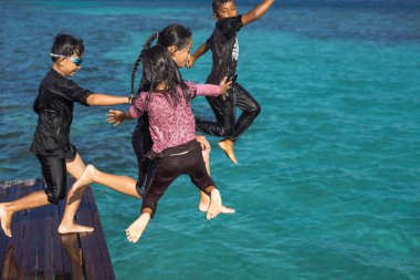 Semporna, Malezya - 26 Kasım 2019: Çocuklar ahşap bir iskeleden suya atlıyorlar.