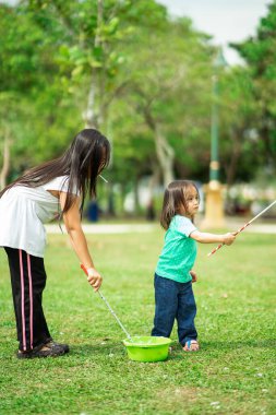 Parkta sabun köpüğüyle oynayan sevimli aktif Asyalı kız kardeşler.