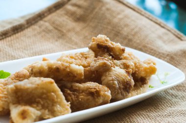 Malezya usulü dövülmüş ve kızartılmış dory balığı küpleri. Kahverengi arka planda uzun bir tabakta servis edilmiş.