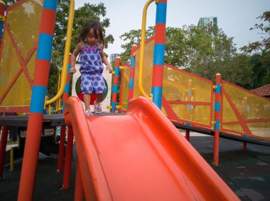 Küçük kız oyun parkında kaydırağın üstünde oynuyor.