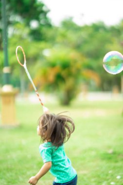 Bahçedeki parkta yüzen sabun köpüğü oynayan çocuğun bulanık fotoğrafı..