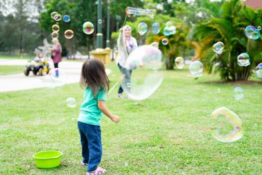 Parkta sabun köpüğüyle oynayan sevimli aktif Asyalı kız. 