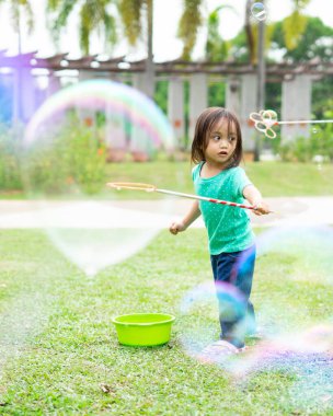 Parkta sabun köpüğüyle oynayan sevimli aktif Asyalı kız. 