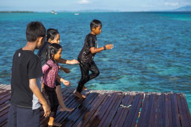 Semporna, Malezya - 26 Kasım 2019: Çocuklar ahşap bir iskeleden suya atlıyorlar.
