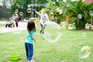 Parkta sabun köpüğüyle oynayan sevimli aktif Asyalı kız. 