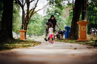Annesi yanında yürürken Asyalı çocuk parkta oynuyor.