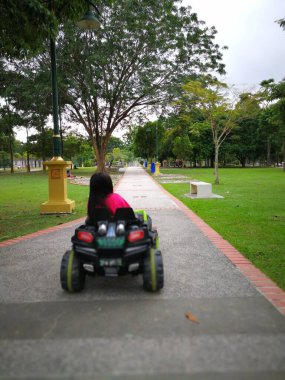 Tropik bir parkta elektrikli oyuncak araba kullanan Asyalı bir çocuk. Açık hava oyuncakları. Pilli araçtaki çocuk. Bahçede oyuncak kamyona binen küçük bir kız. Aile arka bahçede oynuyor..