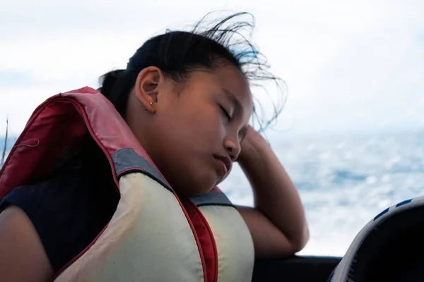 Portrait of an asian young girl sleeping wearing a life jacket in a moving boat.