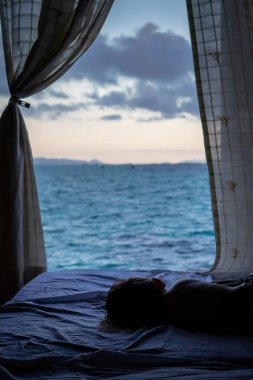 Deniz manzaralı arka plan, çocuklar yatağın üzerinde uyur ve suya bakar..