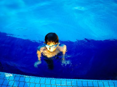 Küçük çocuk havuzda yüzüyor.