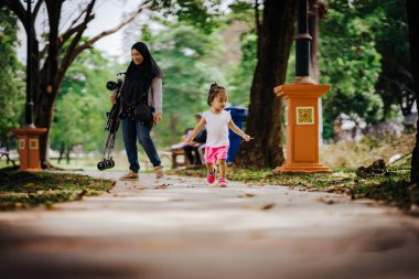 Küçük sevimli Asyalı 2-3 yaşlarında küçük bir kız çocuğu. Arka planda annesiyle parkta yürüyor..