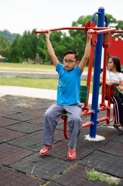 Erkek ve kız kardeş parkta egzersiz makineleriyle çalışıyor.