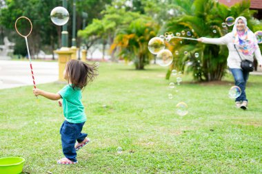 Parkta sabun köpüğüyle oynayan sevimli aktif Asyalı kız. 