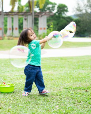 Parkta sabun köpüğüyle oynayan sevimli aktif Asyalı kız. 