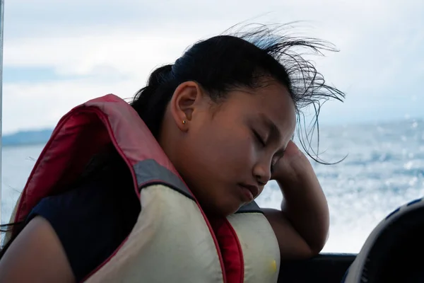 Portrait of an asian young girl sleeping wearing a life jacket in a moving boat.