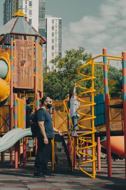 Bangi, Malezya - 18 Eylül 2021 Oyun alanında oynayan küçük kız. Baba çocuğa yardım ediyor..