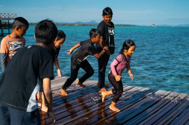 Semporna, Malezya - 26 Kasım 2019: Çocuklar ahşap bir iskeleden suya atlıyorlar.