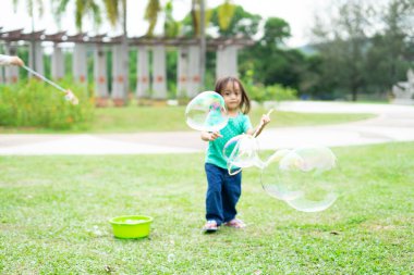 Parkta sabun köpüğüyle oynayan sevimli aktif Asyalı kız.