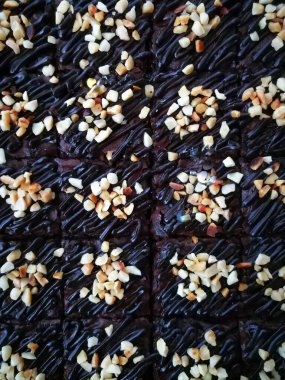 Tahta arka planda, üzerinde badem uçları, ev yapımı fırın ve tatlı olan plastik bir kapta çikolatalı brownie.