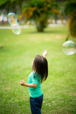 Parkta sabun köpüğüyle oynayan sevimli aktif Asyalı kız.