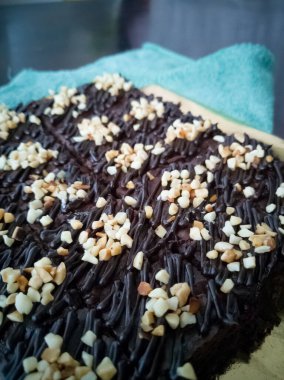 Tahta arka planda, üzerinde badem uçları, ev yapımı fırın ve tatlı olan plastik bir kapta çikolatalı brownie.