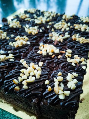 Tahta arka planda, üzerinde badem uçları, ev yapımı fırın ve tatlı olan plastik bir kapta çikolatalı brownie.