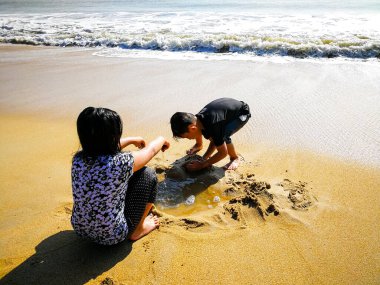 Çocuklar yaz tatilinde plajda oynuyorlar. Çocuklar kumdan kale yapıyorlar.