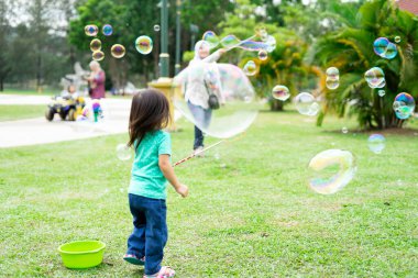 Parkta sabun köpüğüyle oynayan sevimli aktif Asyalı kız.