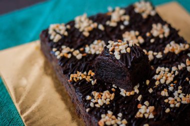 Tahta arka planda, üzerinde badem uçları, ev yapımı fırın ve tatlı olan plastik bir kapta çikolatalı brownie.