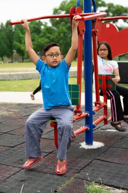 Erkek ve kız kardeş parkta egzersiz makineleriyle çalışıyor.
