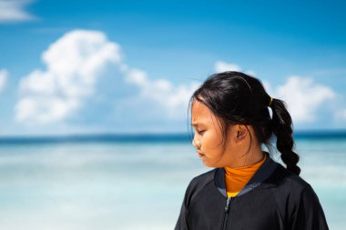 Asyalı çocuk tatillerde plajda oynuyor. Doğada deniz, kum ve mavi gökyüzü olan bir çocuk. Deniz kenarında tatilde olan mutlu genç çocuk suda yürüyor..