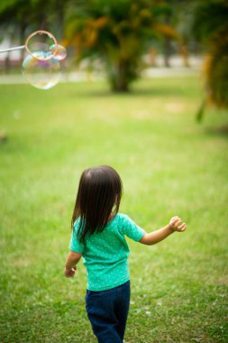 Parkta sabun köpüğüyle oynayan sevimli aktif Asyalı kız.