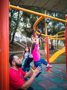 Bangi, Malezya - 18 Ağustos 2019: Babasıyla maymun parmaklıklarındaki çocuk. Spor salonunda takılan küçük bir kız. Çocuklar için sağlıklı bir açık hava aktivitesi. Küçük çocuklar için spor.