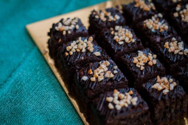 Tahta arka planda, üzerinde badem uçları, ev yapımı fırın ve tatlı olan plastik bir kapta çikolatalı brownie.