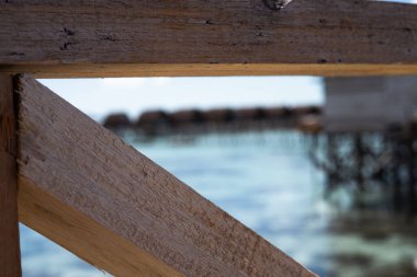 Arka planda bulanık deniz ve su dağ evi olan ahşap köprü korkuluklarını kapatın..