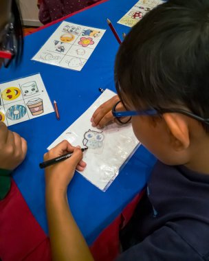 Kuala Lumpur, Malezya - Kasım 2019: Geri dönüşümlü plastik bir konteynır örtüsüne çizim yapan genç bir çocuğun yüksek açılı yakın çekimi. Anahtarlık yapıyorum..