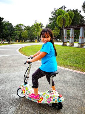 Aktif bir genç kızın portresi. Bir yaz günü parkta scooter sürerken çekilmiş. Mevsimlik çocuk aktivitesi sporu. Sağlıklı çocukluk yaşam tarzı