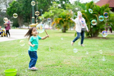 Parkta sabun köpüğüyle oynayan sevimli aktif Asyalı kız.