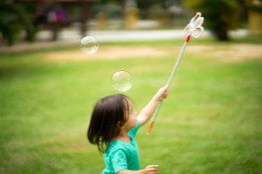 Bahçedeki parkta yüzen sabun köpüğü oynayan çocuğun bulanık fotoğrafı..