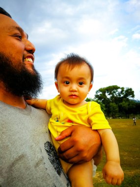 Parkta babası tarafından taşınan 9 aylık tatlı Asyalı bebek. Sakallı baba şefkatle bir bebek tutuyor. Seçici odak.