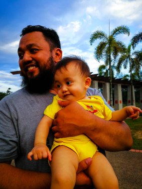 Parkta babası tarafından taşınan 9 aylık tatlı Asyalı bebek. Sakallı baba şefkatle bir bebek tutuyor. Seçici odak.