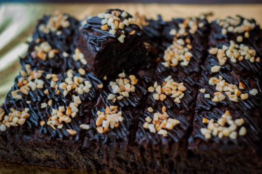 Tahta arka planda, üzerinde badem uçları, ev yapımı fırın ve tatlı olan plastik bir kapta çikolatalı brownie.