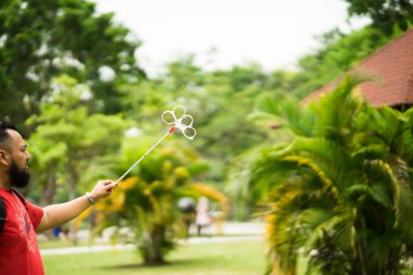 Bangi, Malezya - 6 Ekim 2019: Sakallı adam parkta sabun köpüğü oynuyor.