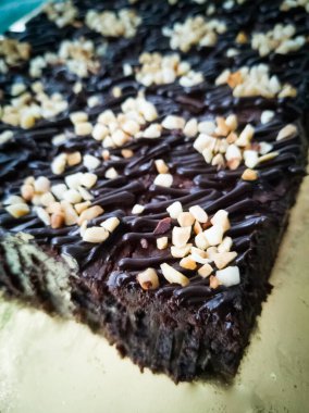 Tahta arka planda, üzerinde badem uçları, ev yapımı fırın ve tatlı olan plastik bir kapta çikolatalı brownie.